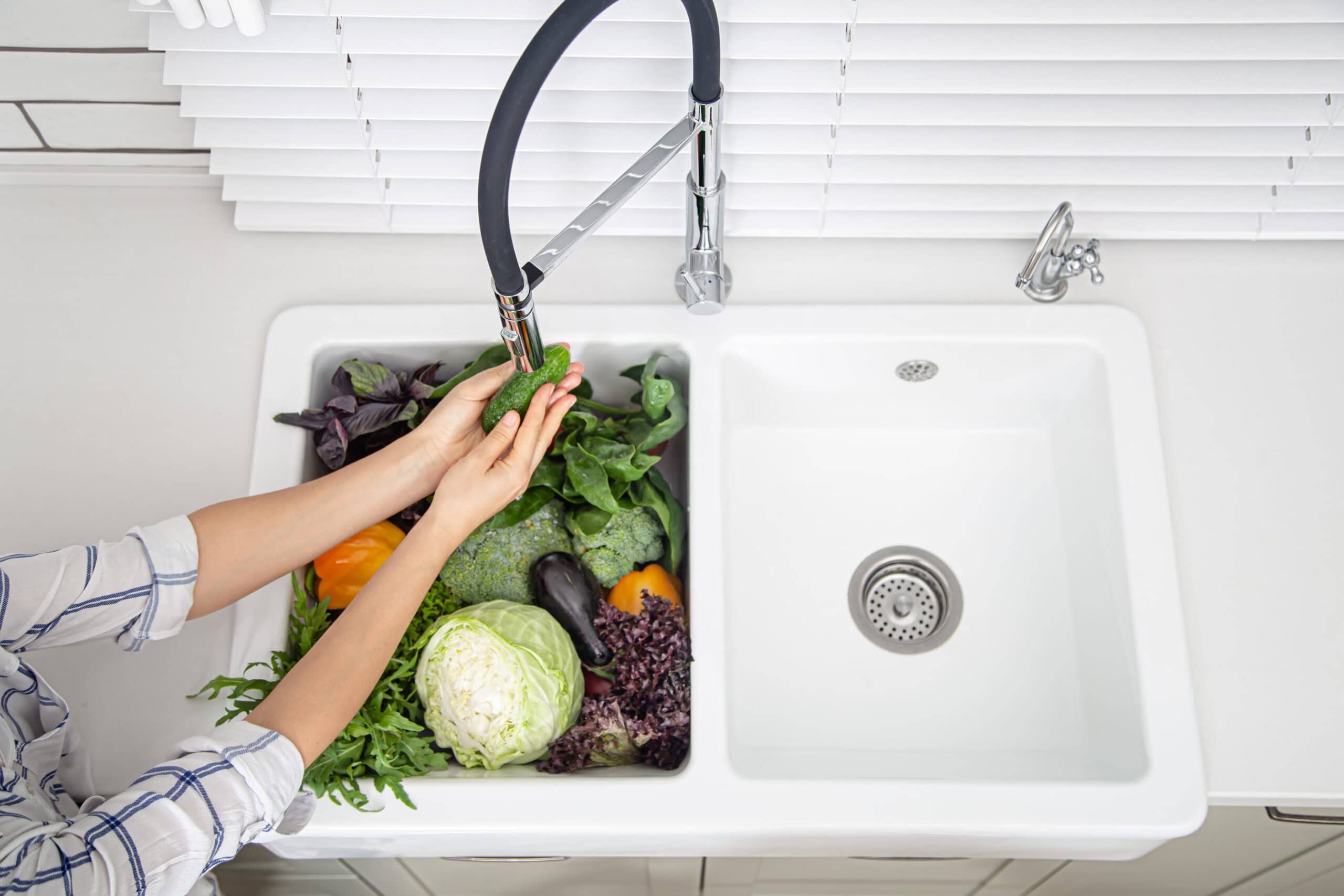 Female hands washing vegetables in the kitchen sink of modern kitchen top view